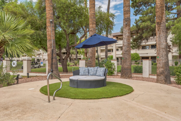A serene outdoor seating area invites relaxation, surrounded by lush greenery and gentle shade.