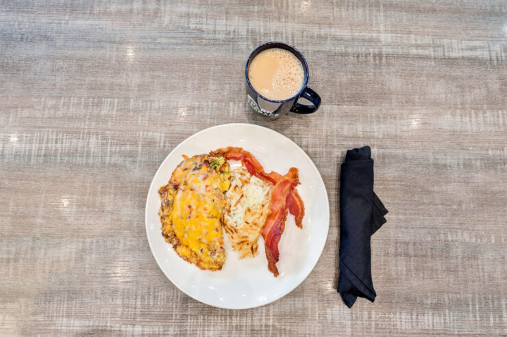 A warm breakfast plate featuring hearty eggs, crispy bacon, and a comforting cup of coffee awaits.