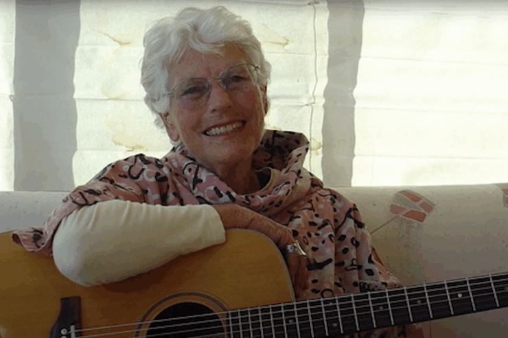 A smiling woman holds a guitar, radiating warmth in a bright, inviting space, fostering community spirit.