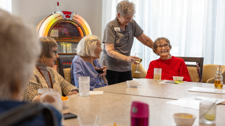 Residents engage joyfully around a table, sharing drinks and laughter in a welcoming atmosphere.