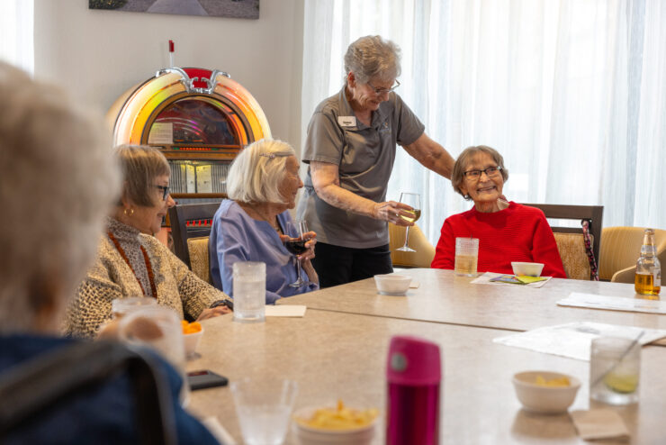 Residents engage joyfully around a table, sharing drinks and laughter in a welcoming atmosphere.