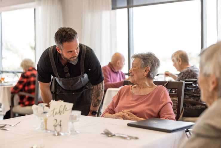 A warm dining atmosphere where friendly staff engage with residents, fostering community and joy.