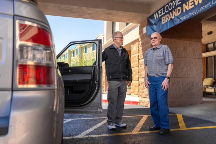 Two gentlemen stand together outside a welcoming retirement community, enjoying a friendly conversation.