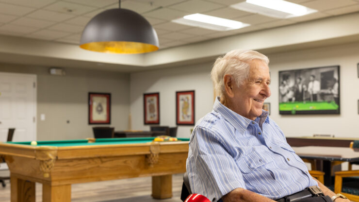 A cheerful resident enjoys a game room, fostering connection and warmth in a welcoming community.