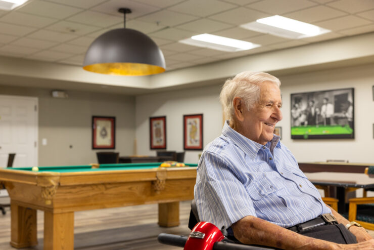 A cheerful resident enjoys a game room, fostering connection and warmth in a welcoming community.