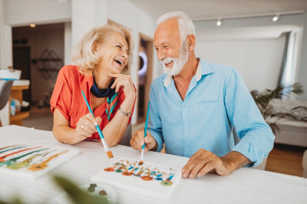 A joyful couple shares laughter while painting together, embodying community and creativity.