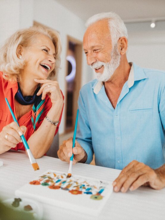 A joyful couple shares laughter while painting together, embodying community and creativity.