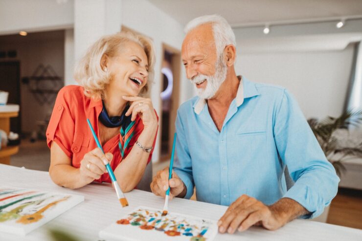 A joyful couple shares laughter while painting together, embodying community and creativity.