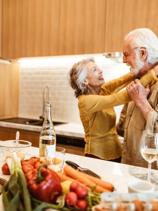 A joyful couple shares a tender moment in a bright kitchen, surrounded by fresh produce and warmth.