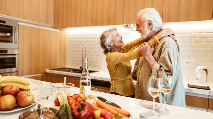 A joyful couple shares a tender moment in a bright kitchen, surrounded by fresh produce and warmth.