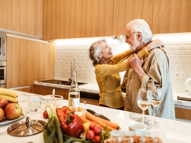 A joyful couple shares a tender moment in a bright kitchen, surrounded by fresh produce and warmth.