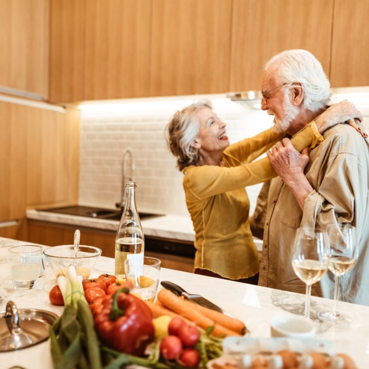 A joyful couple shares a tender moment in a bright kitchen, surrounded by fresh produce and warmth.