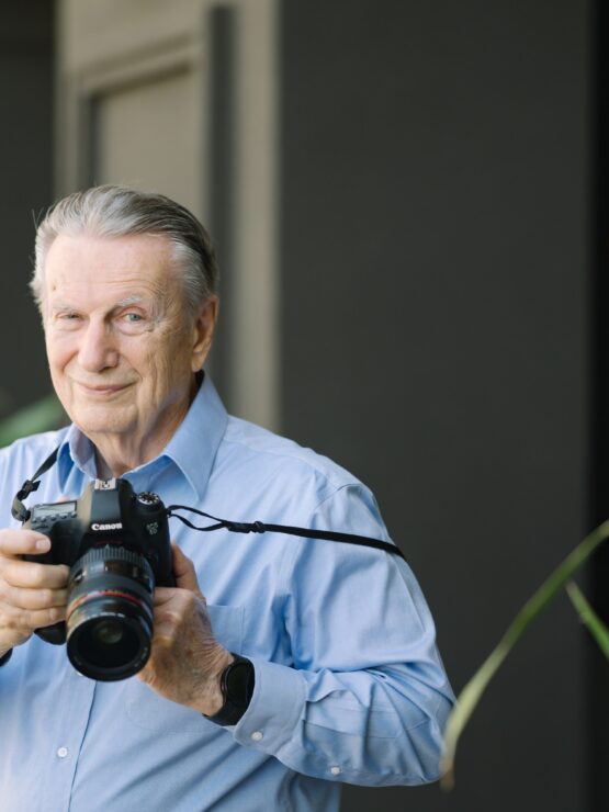 A friendly resident captures moments with a camera, surrounded by vibrant plants, reflecting community spirit.