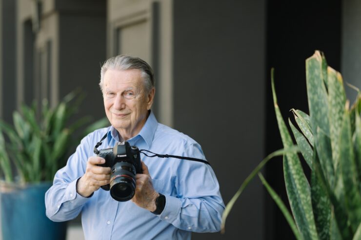 A friendly resident captures moments with a camera, surrounded by vibrant plants, reflecting community spirit.