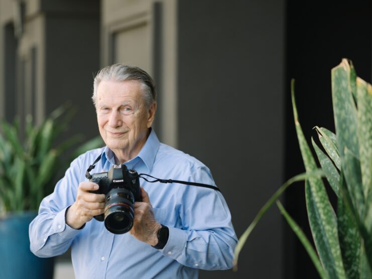 A friendly resident captures moments with a camera, surrounded by vibrant plants, reflecting community spirit.
