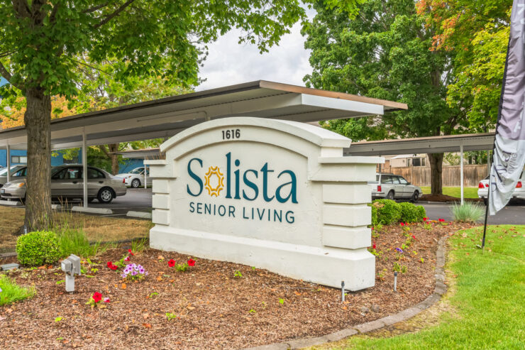 Welcoming sign at Solista Senior Living, surrounded by lush greenery and vibrant flowers, inviting community.
