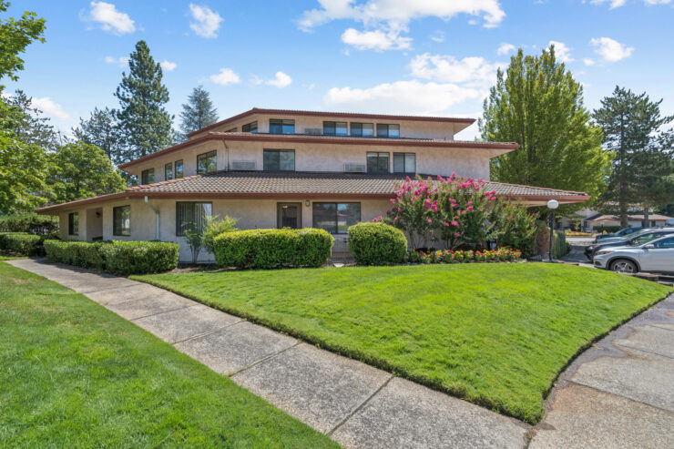 A welcoming retirement community surrounded by lush greenery and vibrant flowers, inviting connection.
