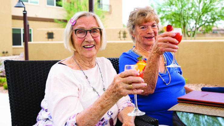 Two joyful women celebrate together, raising their drinks in a warm, inviting outdoor setting.
