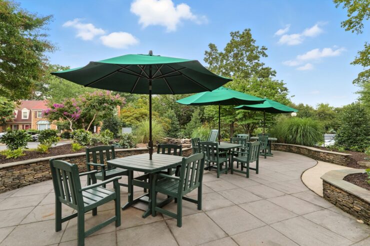 A serene outdoor patio with green umbrellas, inviting seating, and lush greenery fosters community and relaxation.
