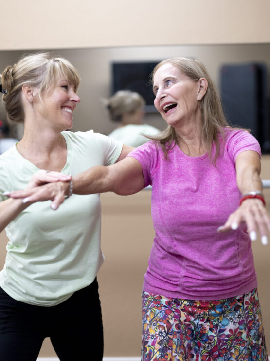 Two women joyfully engage in a dance class, embodying community spirit and vibrant energy.