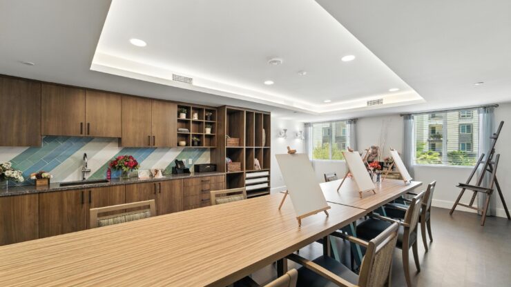 A bright, inviting art room featuring a spacious table, easels, and warm wooden accents, perfect for community gatherings.