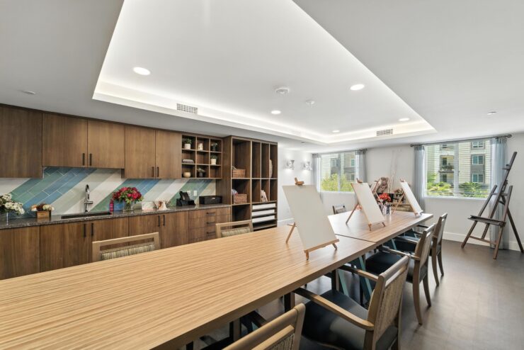 A bright, inviting art room featuring a spacious table, easels, and warm wooden accents, perfect for community gatherings.