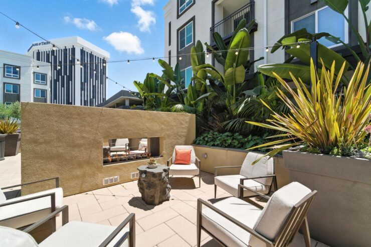 A serene outdoor lounge features comfortable seating, lush greenery, and inviting warmth, perfect for community gatherings.