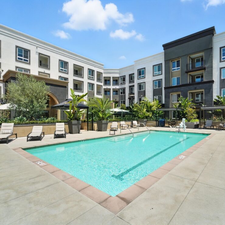 A serene pool area surrounded by lush greenery and comfortable lounge chairs invites relaxation and community.