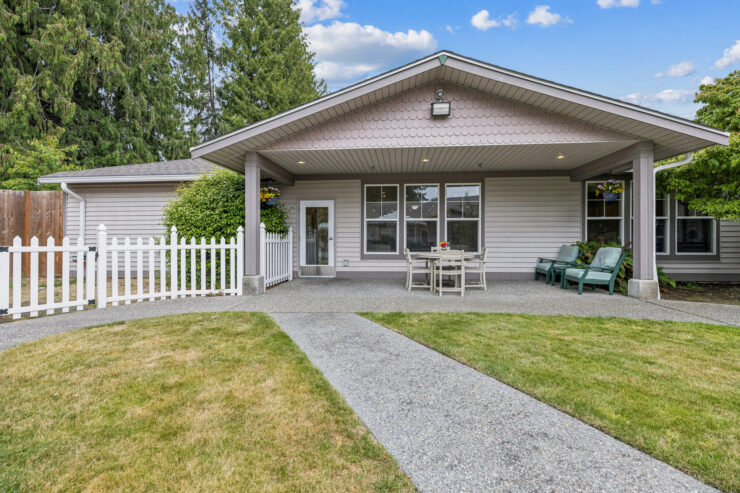 A welcoming patio features seating and a table, surrounded by lush greenery, inviting relaxation and community.