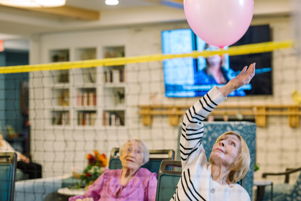 Residents engage joyfully in a lively balloon game, fostering connection and laughter in a warm community space.