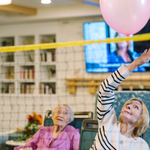 Residents engage joyfully in a lively balloon game, fostering connection and laughter in a warm community space.