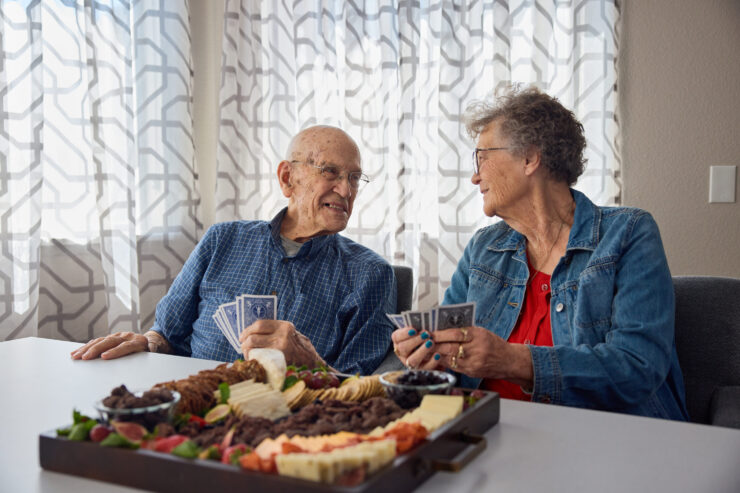 Two residents share laughter and friendly conversation over a card game, enjoying a delightful spread.