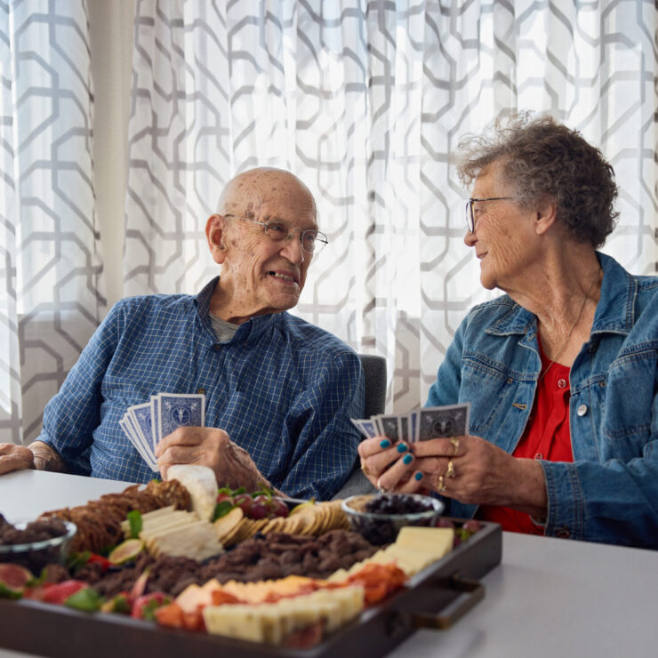 Two residents share laughter and friendly conversation over a card game, enjoying a delightful spread.