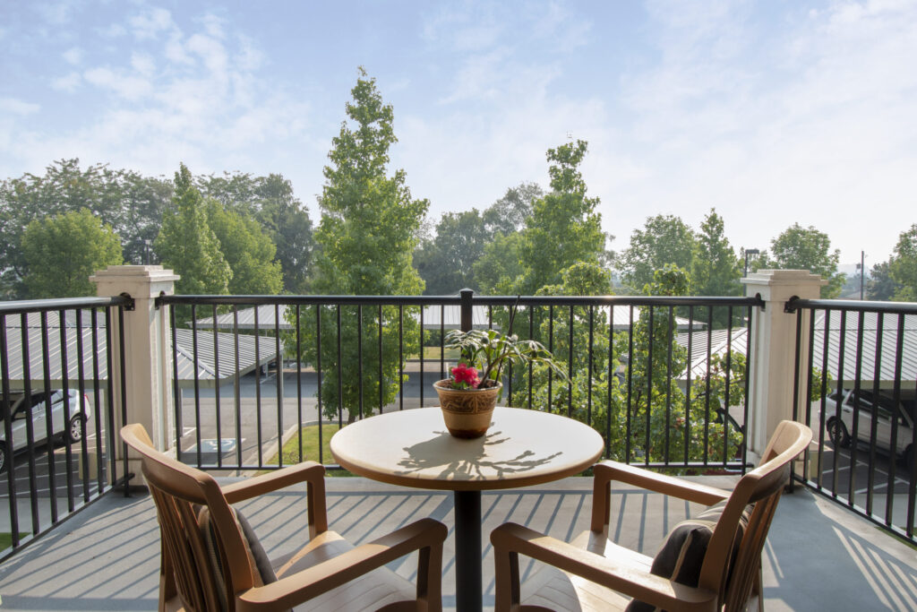 A serene balcony offers a perfect spot for relaxation, surrounded by lush greenery and gentle sunlight.