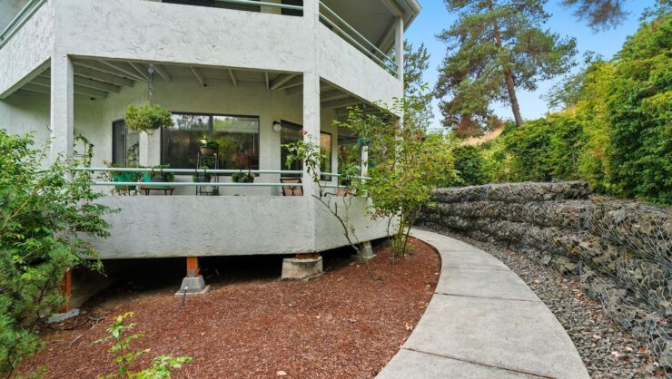 A serene pathway leads to a welcoming patio, surrounded by lush greenery, fostering a sense of community and comfort.