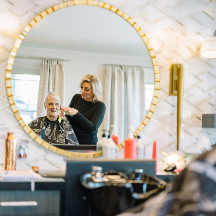 A cheerful atmosphere is captured as a stylist attentively cuts a resident's hair, showcasing community care.