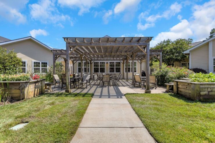 Outdoor seating area with shaded pergola, surrounded by well-maintained gardens and greenery.