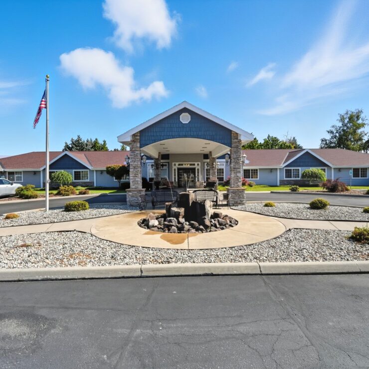Well-maintained retirement home exterior with seating areas and landscaped grounds under a clear sky.