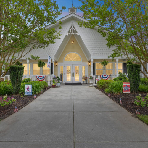 Welcoming entrance to a bright, charming community with lush landscaping and patriotic décor.
