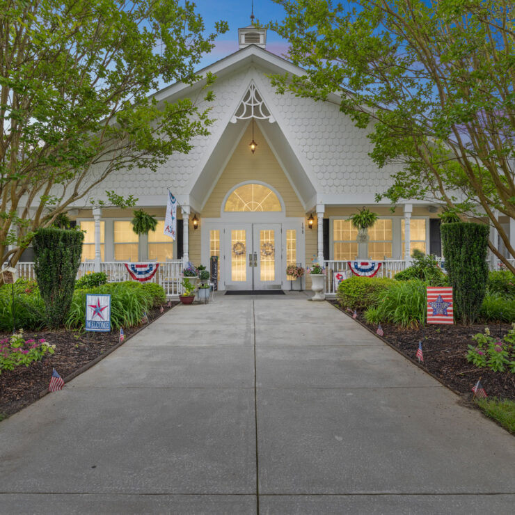 Welcoming entrance to a bright, charming community with lush landscaping and patriotic décor.