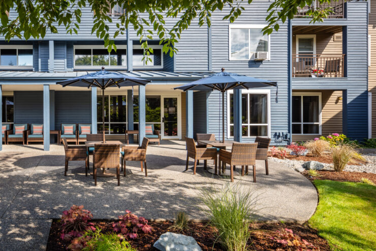 Outdoor patio seating with umbrellas at a retirement community surrounded by greenery and flowers.