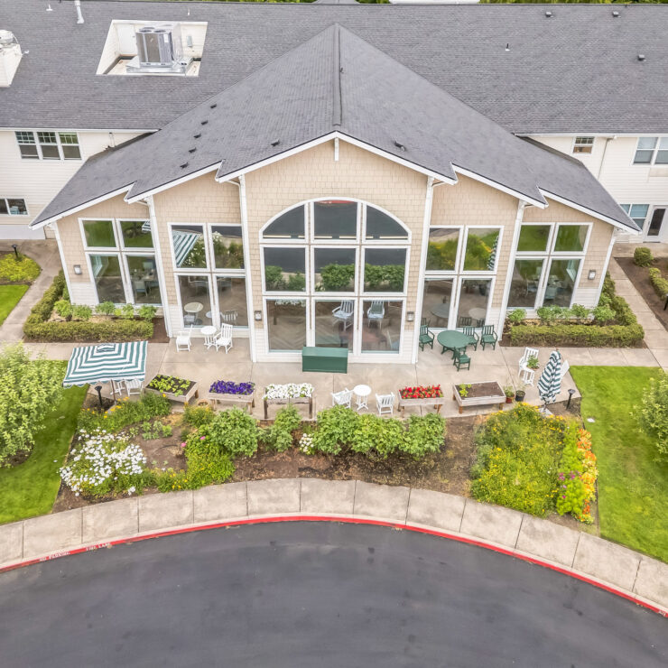 Sunlit retirement home exterior with garden seating, colorful flowers, and lush greenery.