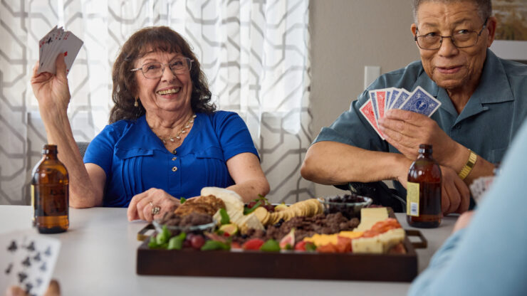 Seniors enjoying a friendly card game with snacks and drinks in a welcoming community space.
