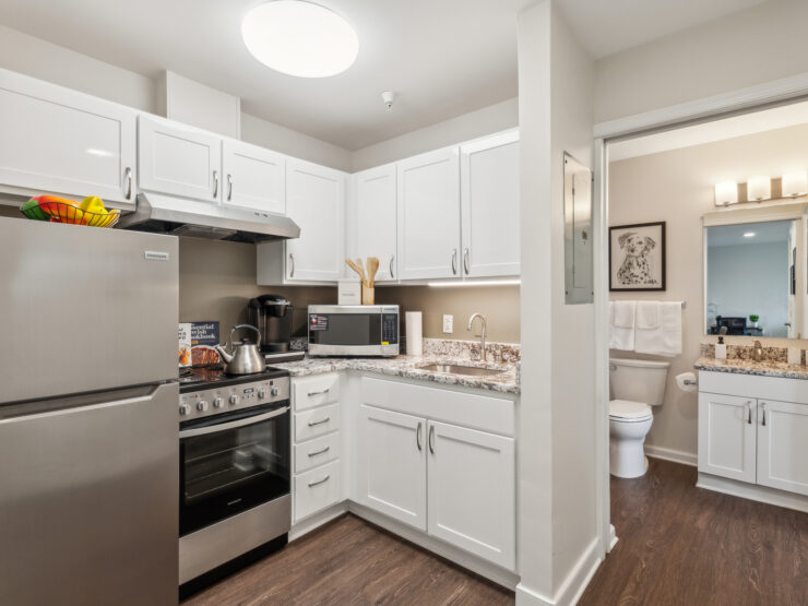 Bright, modern kitchen with clean white cabinetry and stainless steel appliances next to a well-lit bathroom.