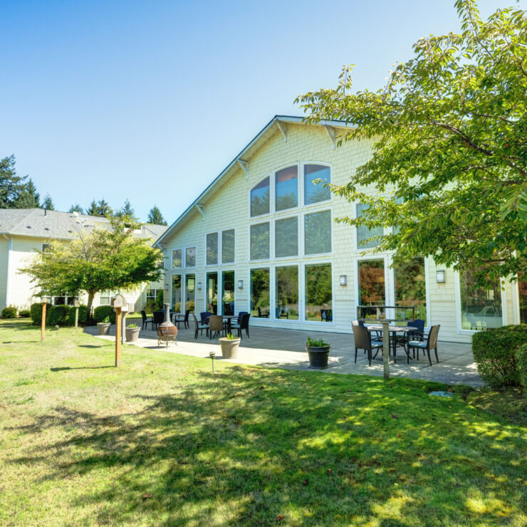 Sunlit outdoor patio with seating and lush green lawn at a welcoming retirement community.