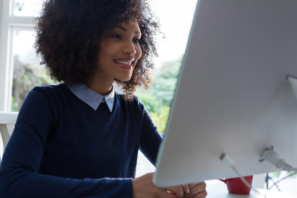 A cheerful woman engages with her computer, surrounded by natural light, fostering a sense of connection and warmth.