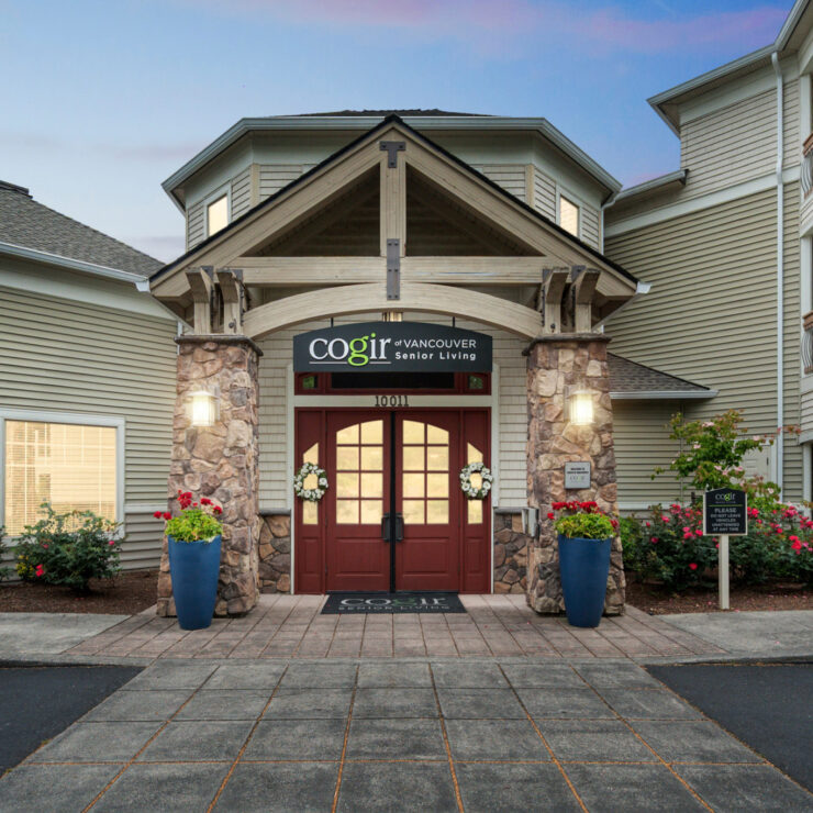 Welcoming entrance to a senior living community surrounded by flowers and warm lighting.