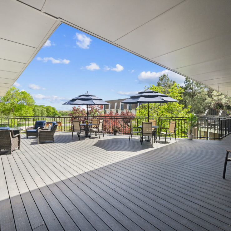 Spacious outdoor patio with comfortable seating and shaded tables overlooking lush greenery.