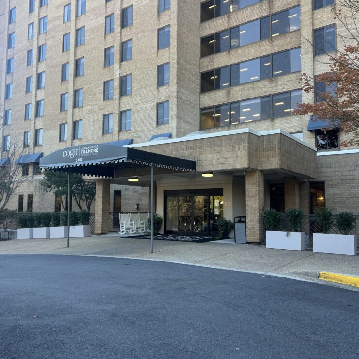 Entrance to a senior living community with rocking chairs and greenery enhancing a welcoming environment.