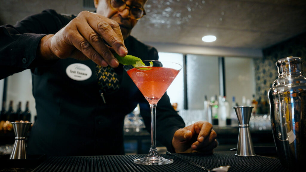 A bartender skillfully garnishes a vibrant cocktail, creating a welcoming atmosphere for residents.